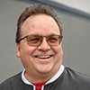 Smiling middle aged white man with glasses standing in front of grey wall