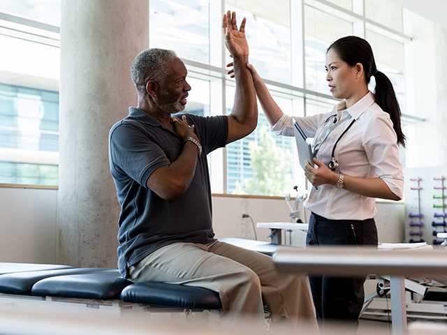 Medical provider helping man raise arm.