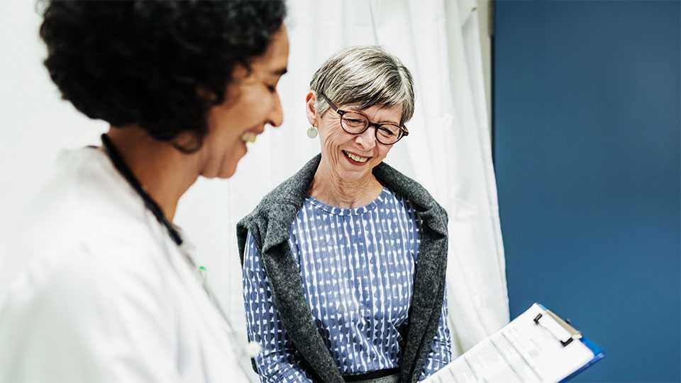 female doctor wearing a lab coat standing next to smiling woman as they look at paperwork