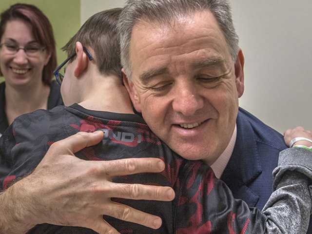 Man hugging child while woman looks on smiling.